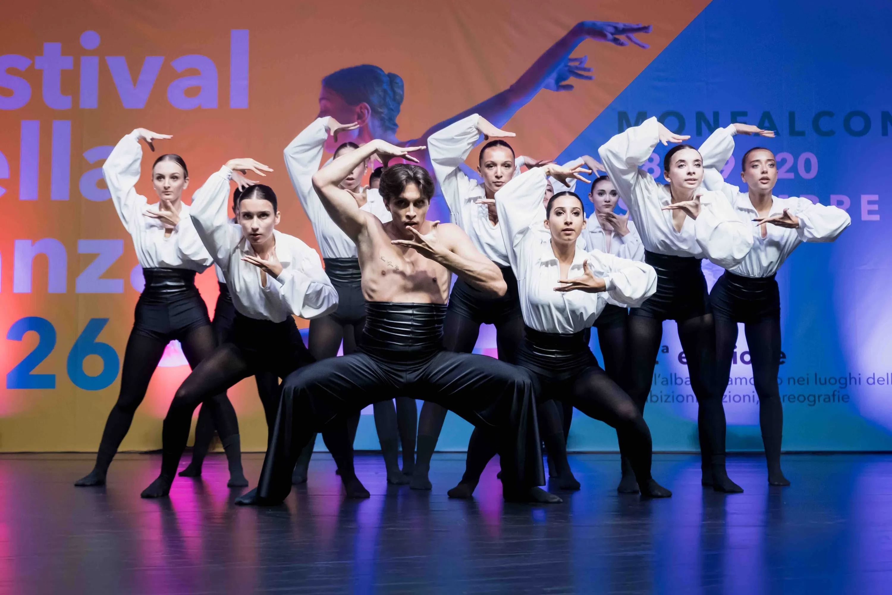 Gruppo di danzatori in camicia bianca in posa davanti al fondale del festival