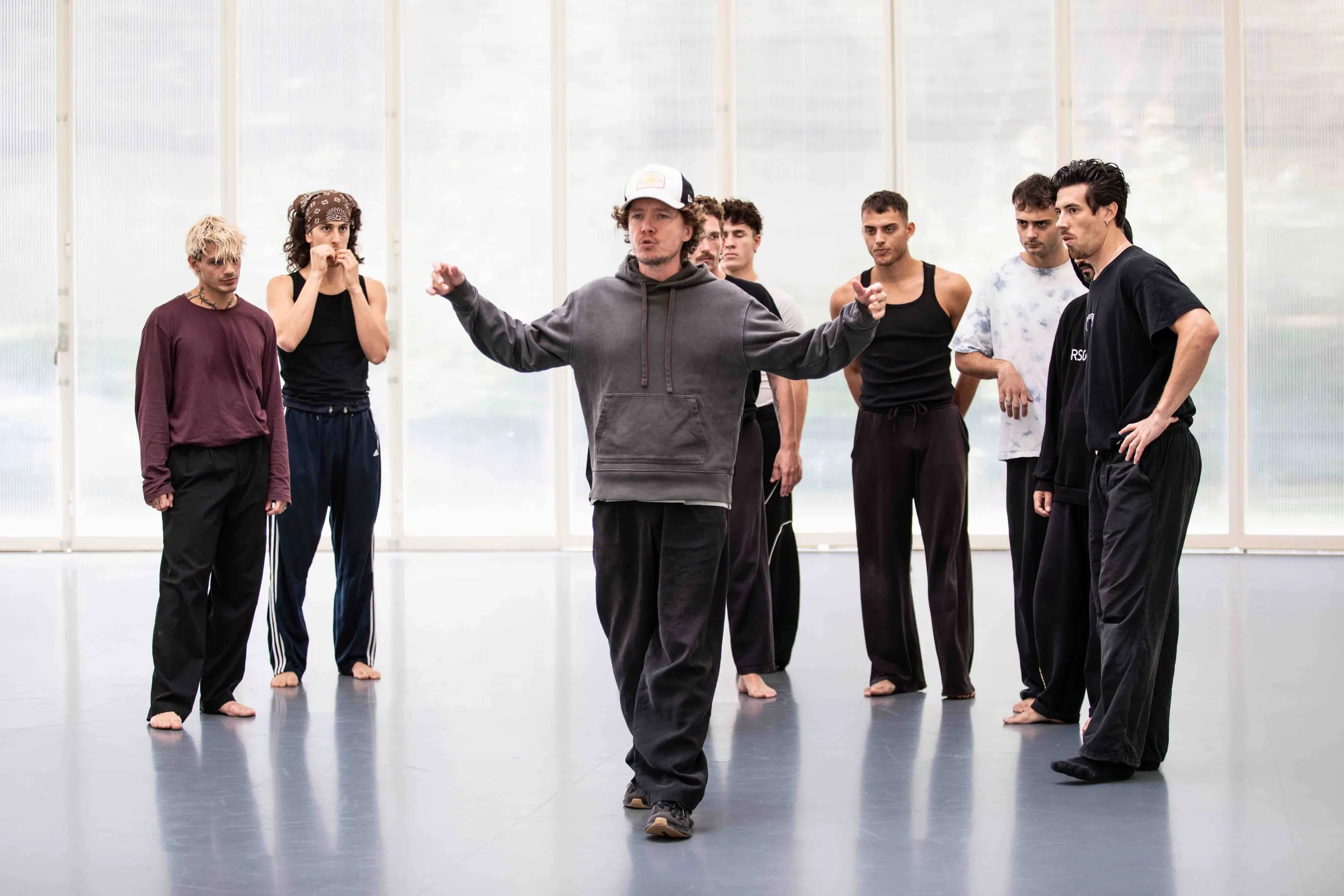 Il gruppo di danzatori ascolta il coreografo in una sala luminosa