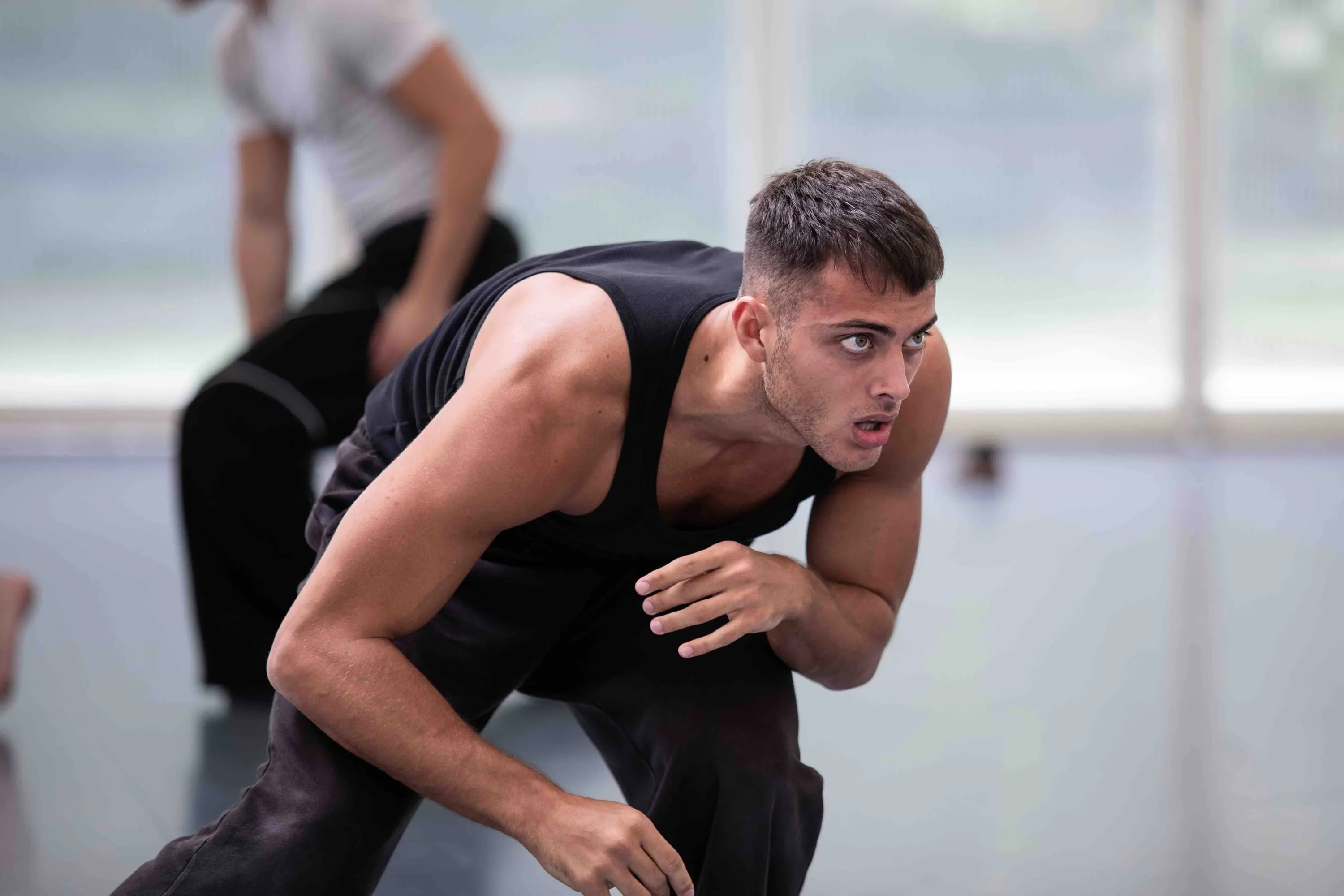 Un danzatore in canottiera nera piegato in avanti, concentrato