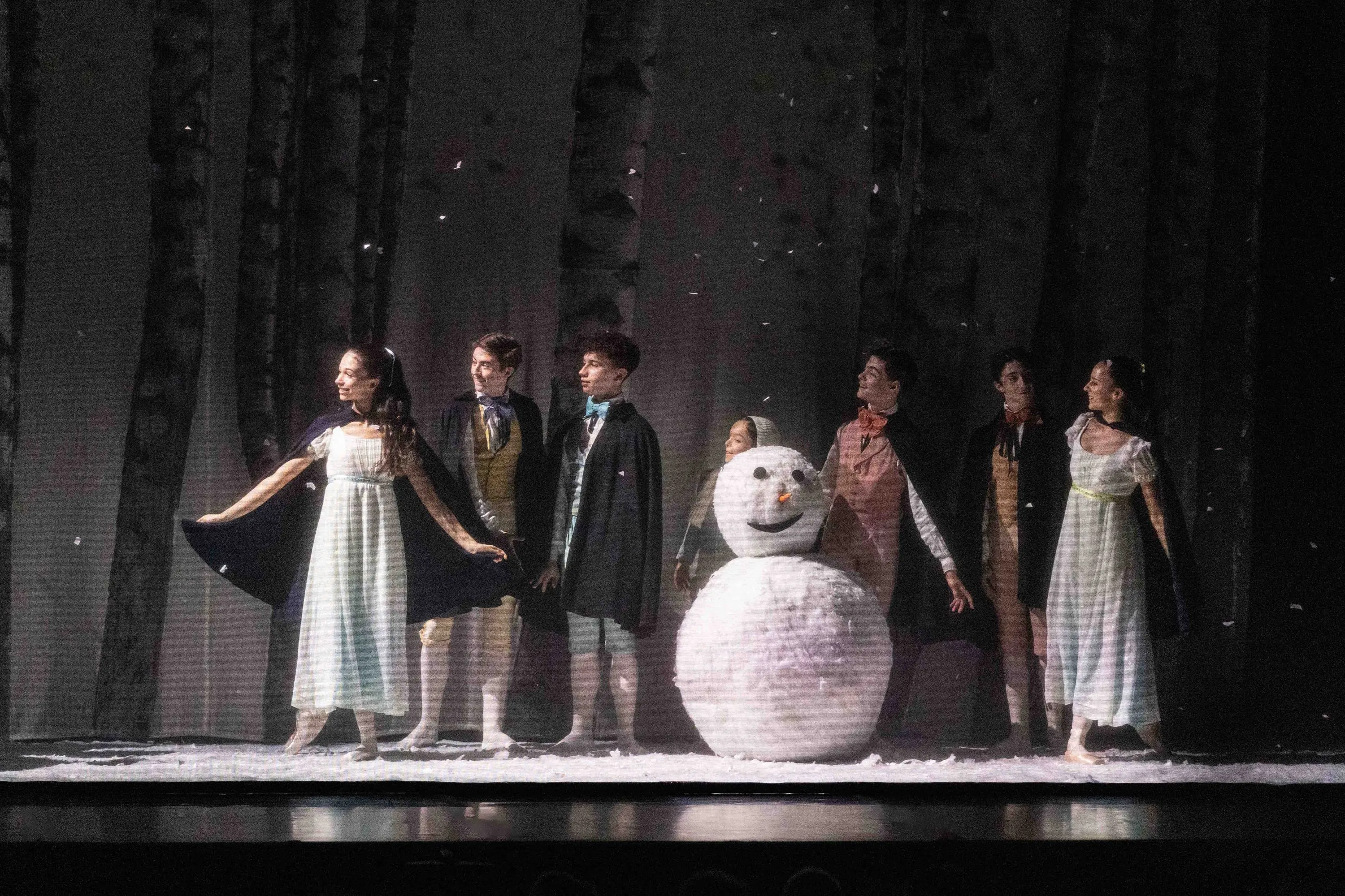 Scena sulla neve con un pupazzo di neve e giovani interpreti in costume