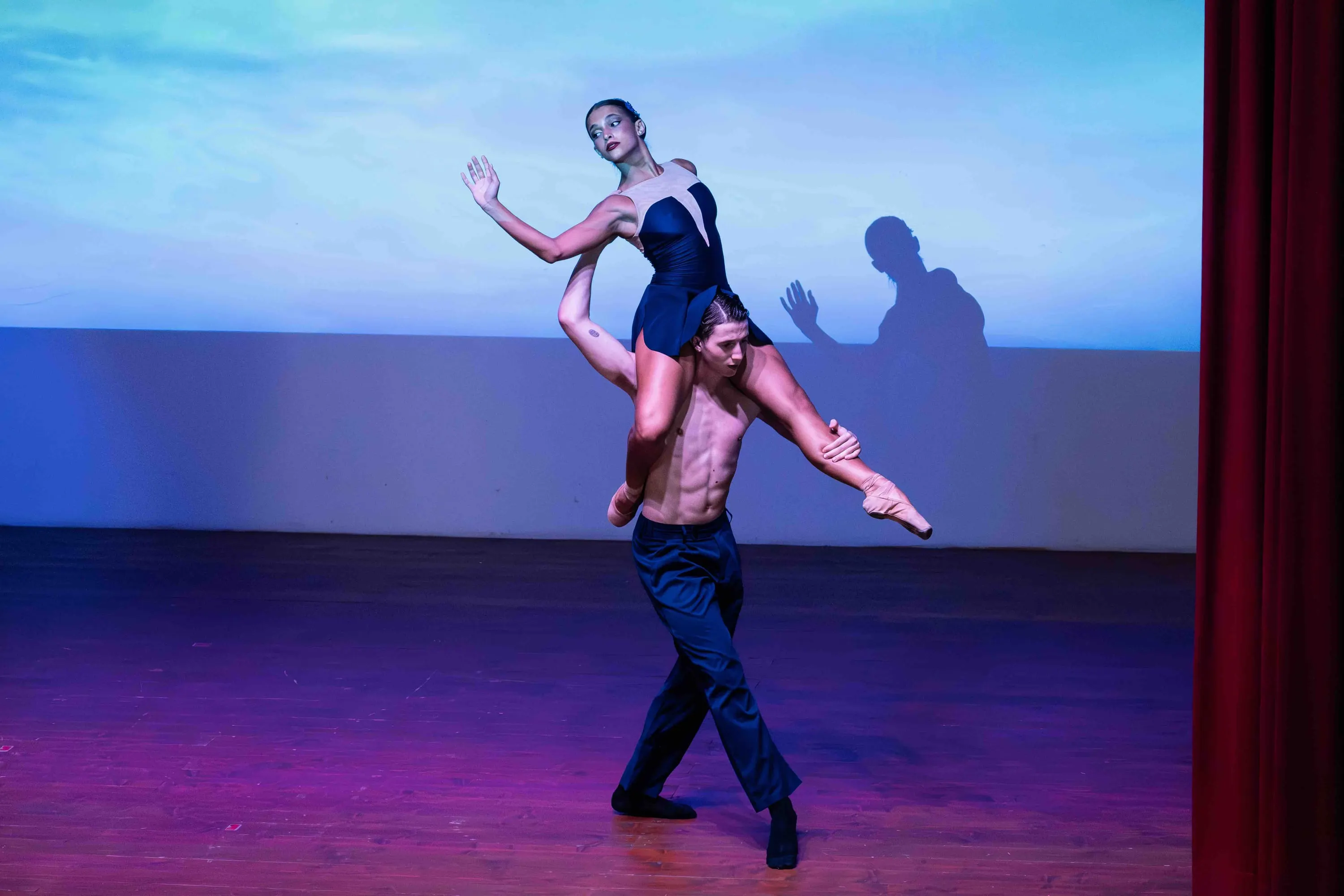 Un danzatore regge sulle spalle una ballerina, in luce blu