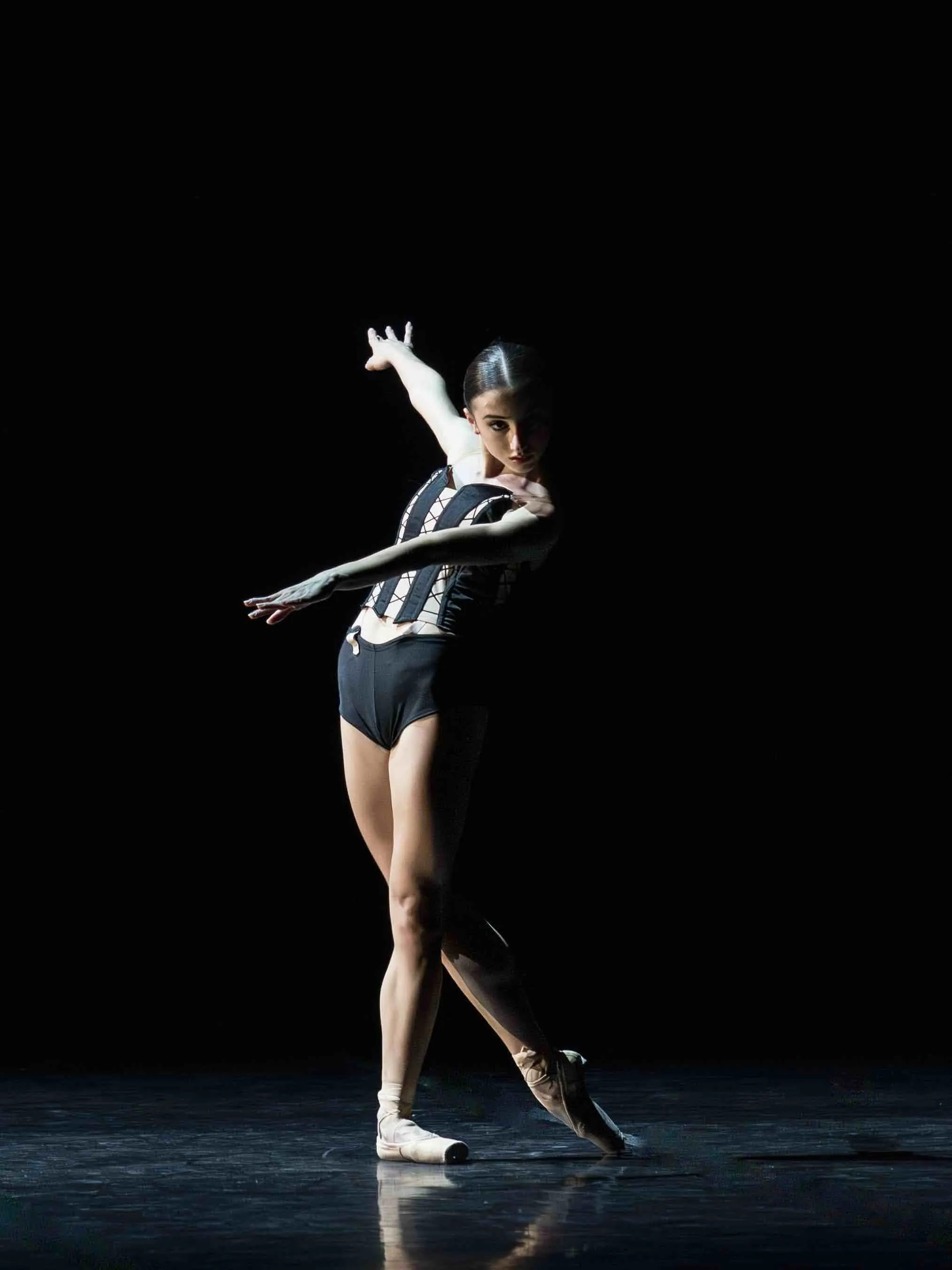 Una ballerina in body a righe in equilibrio sulle punte, su fondo nero